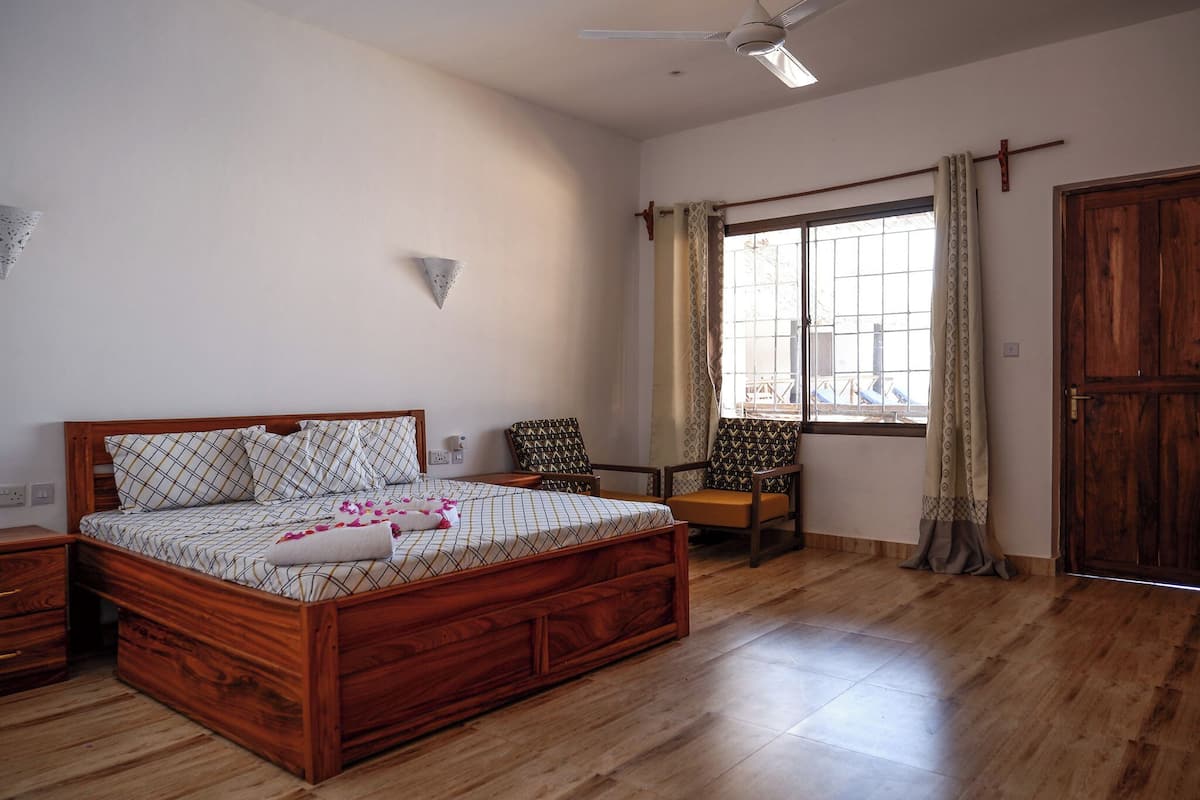 Un dormitorio con cama de madera, mesita de noche, silla, ventana con cortinas y puerta.