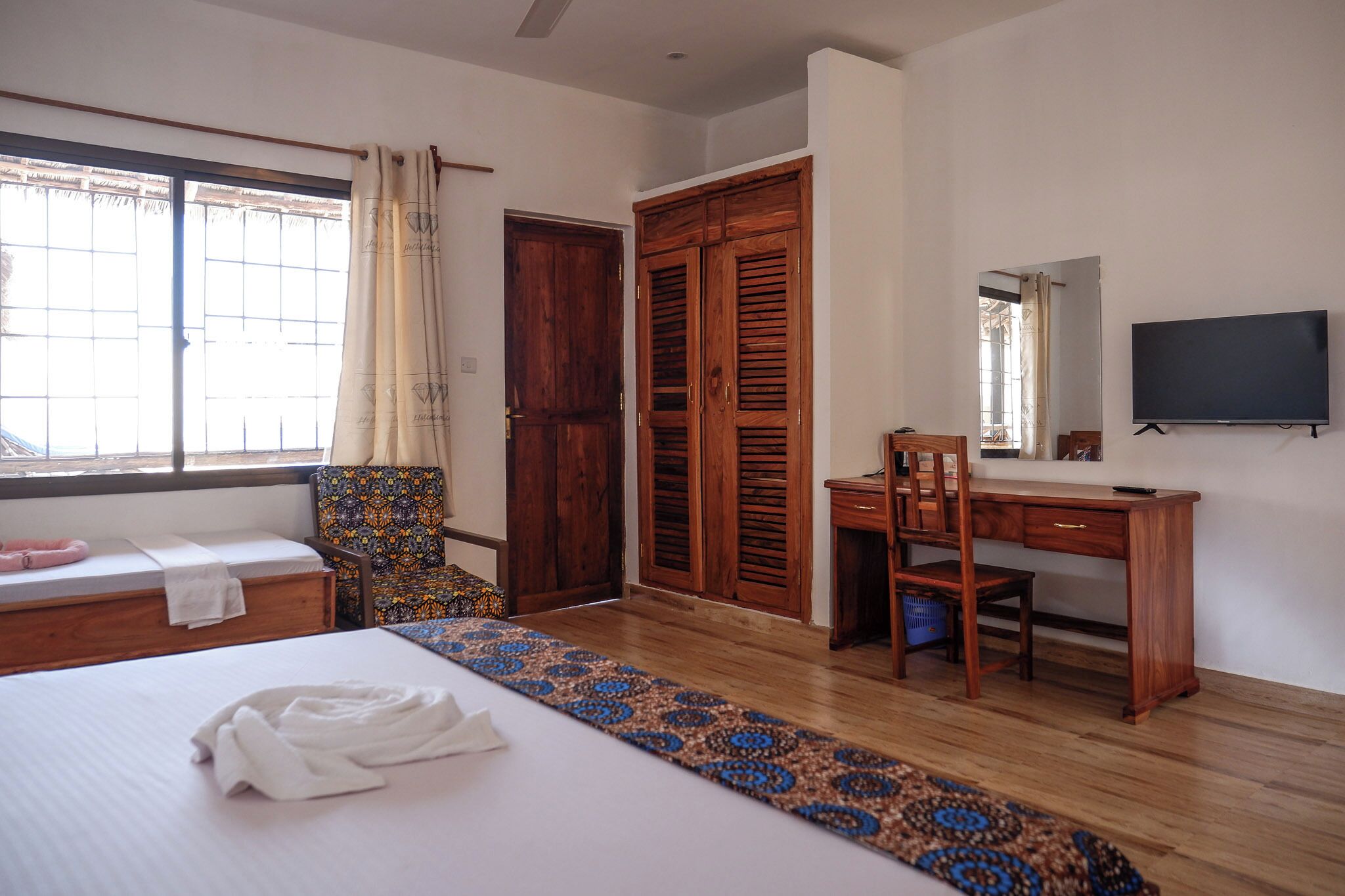 A hotel room with a bed, a desk, a chair, a wardrobe, and a TV.