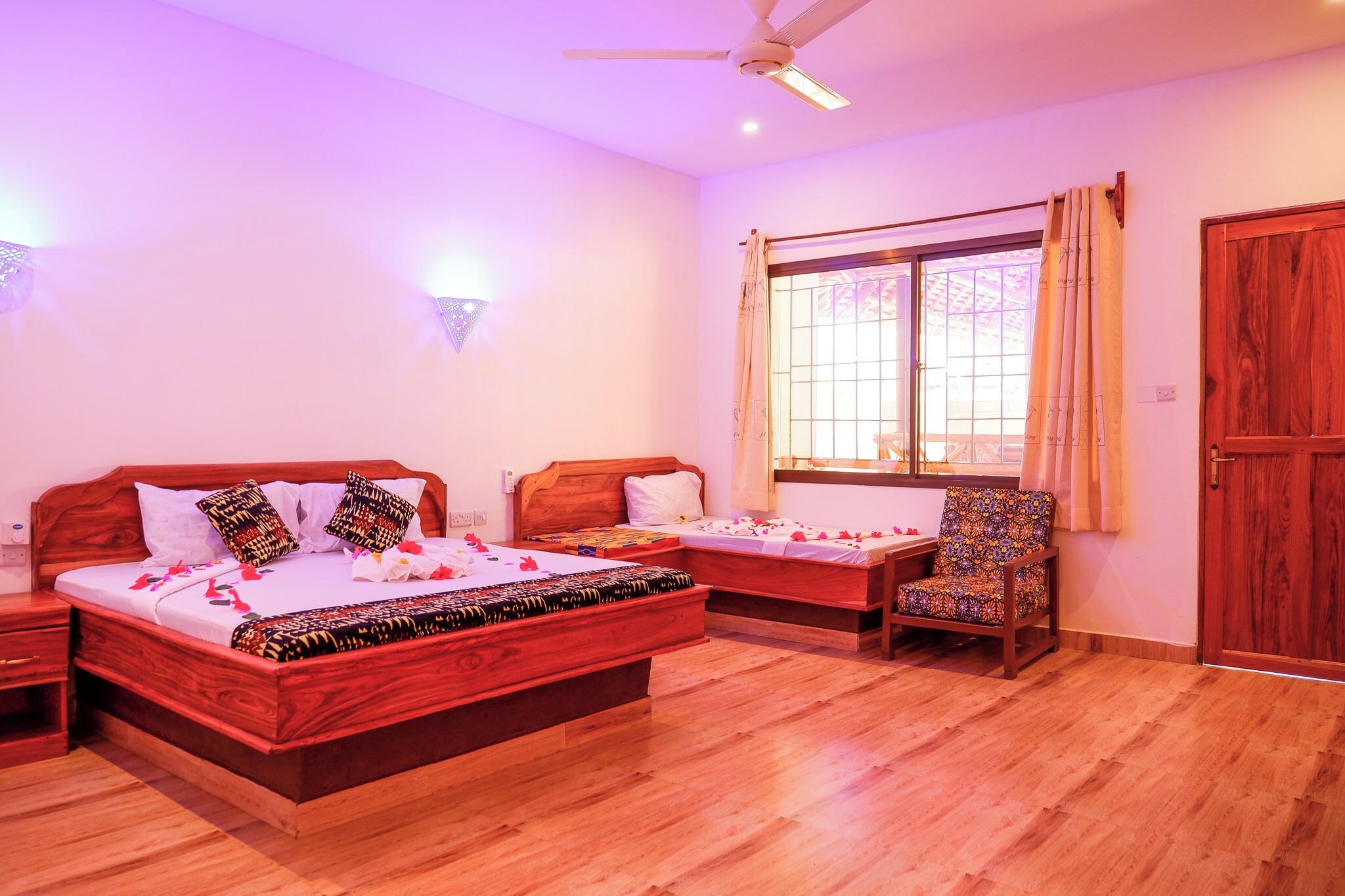 A bedroom with a large bed, a smaller bed, a chair, a wardrobe, and a window with curtains.