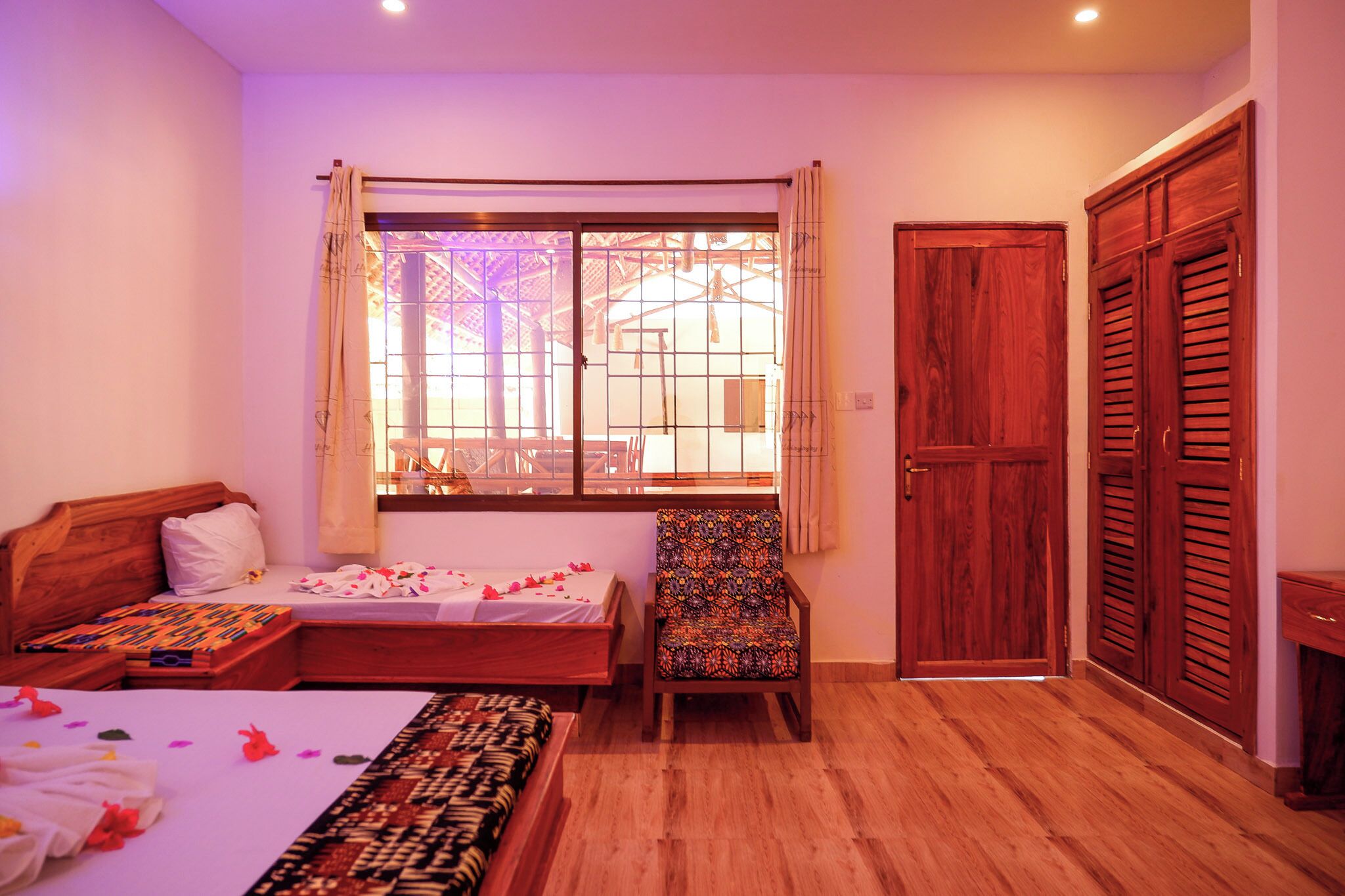 A room with a bed, a chair, a window with curtains, and wooden doors.