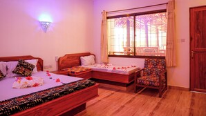 Une chambre d’hôtel avec deux lits en bois, une chaise en bois, une fenêtre avec des rideaux et un luminaire fixé au mur.