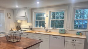 A modern kitchen with white cabinetry, a wooden countertop, a dishwasher, and a window with a view of trees.