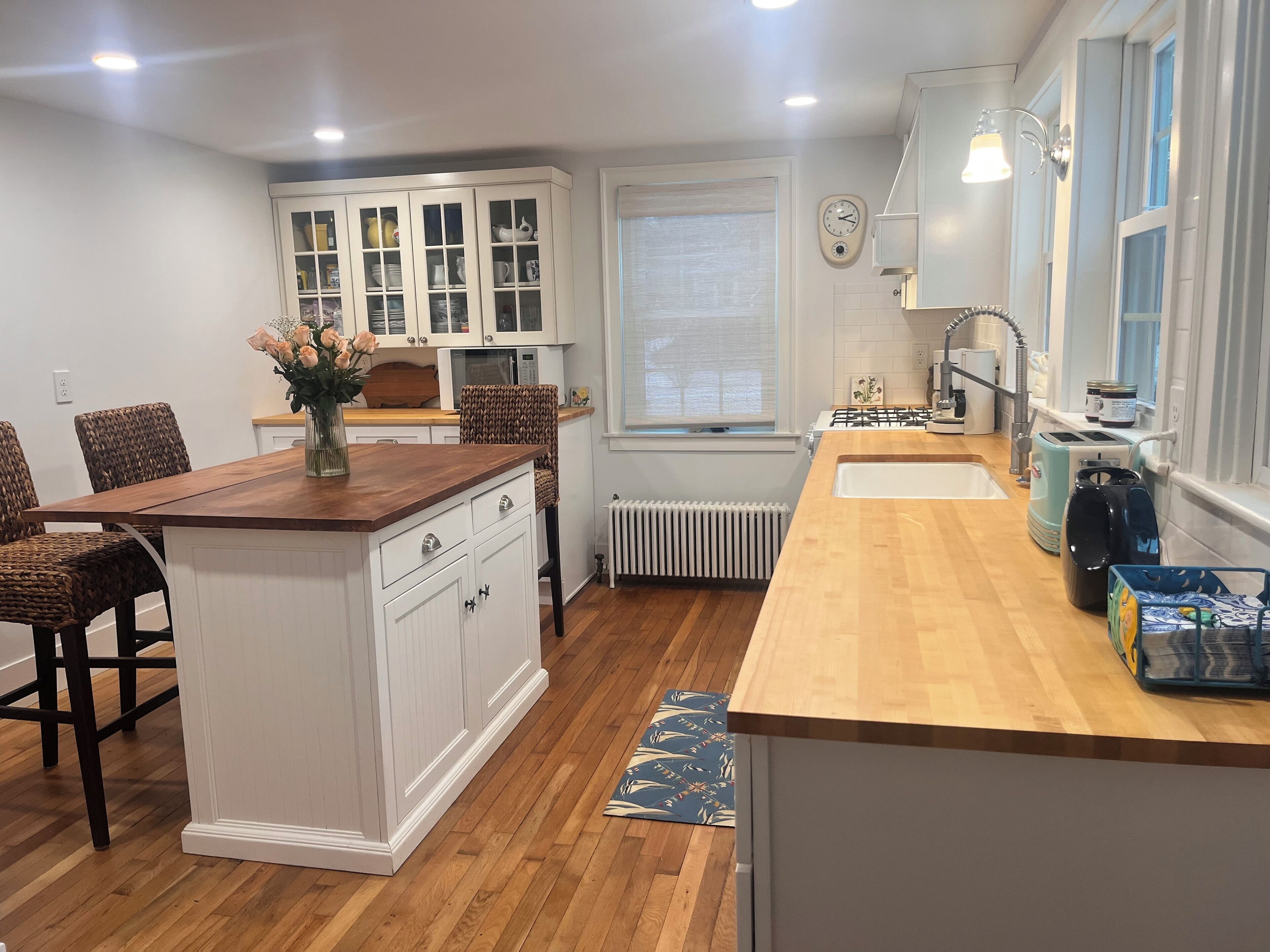 Une cuisine moderne avec des meubles blancs, un îlot central en bois et un four à micro-ondes encastré.