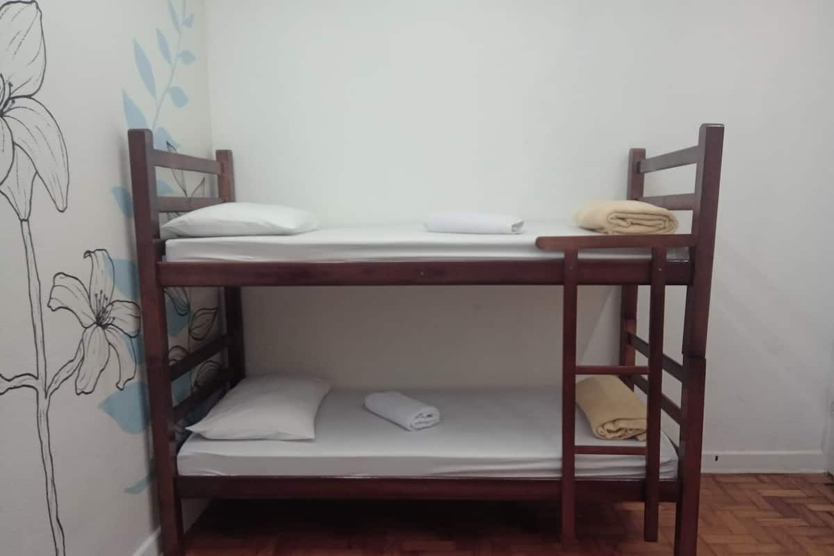 A bunk bed with white bedding and pillows, a wooden ladder, and a floral wall design.