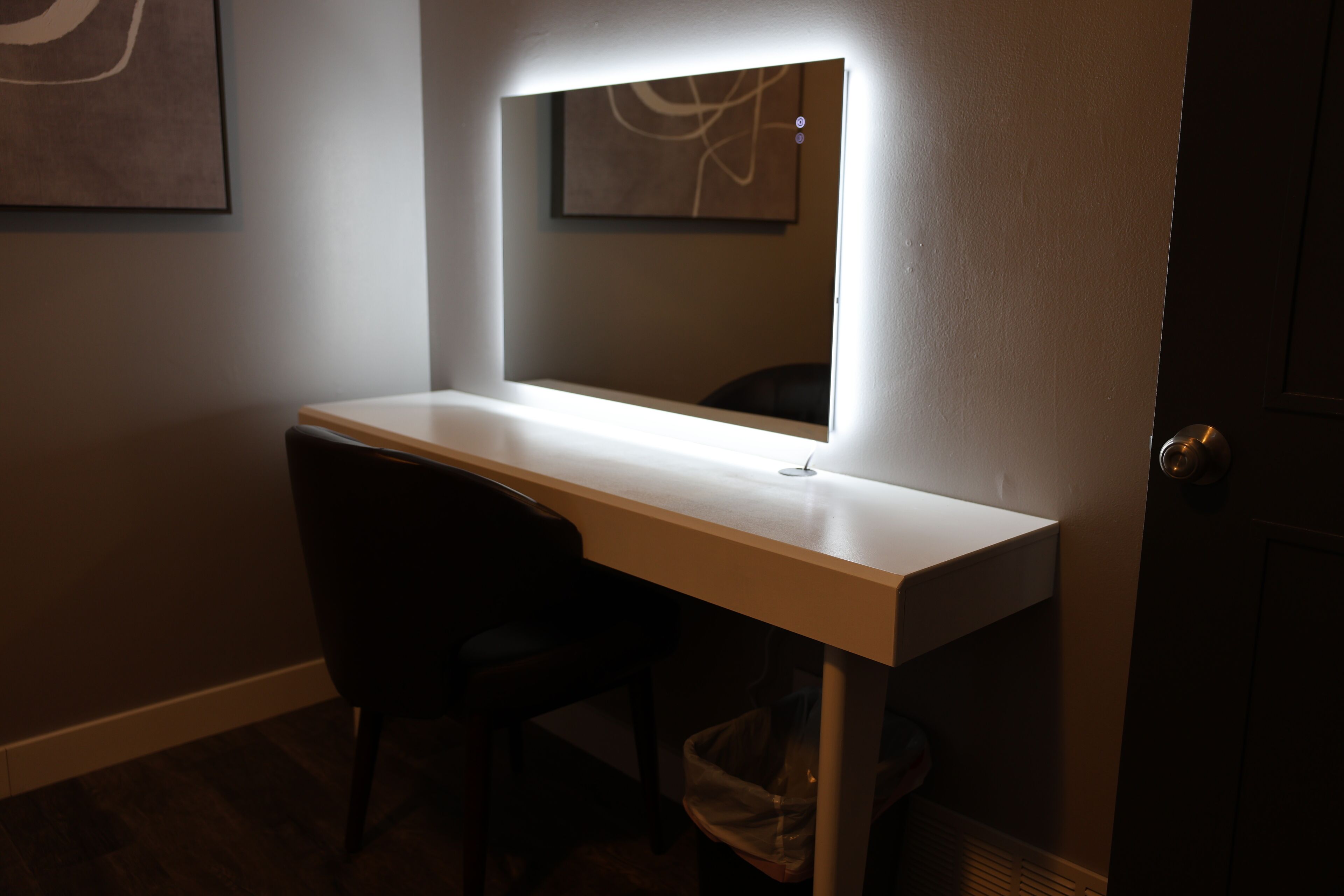 Un bureau avec un miroir et une chaise, dans une pièce à la lumière tamisée.