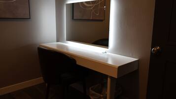 Un bureau avec un miroir et une chaise, dans une pièce à la lumière tamisée.