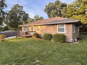 A single-story house with a sloped roof, a front porch, and a well-maintained lawn. - Heartland Haven in Kansas City Area: Pet Friendly -fenced yard &Newly Remodeled! (Sugar Creek)