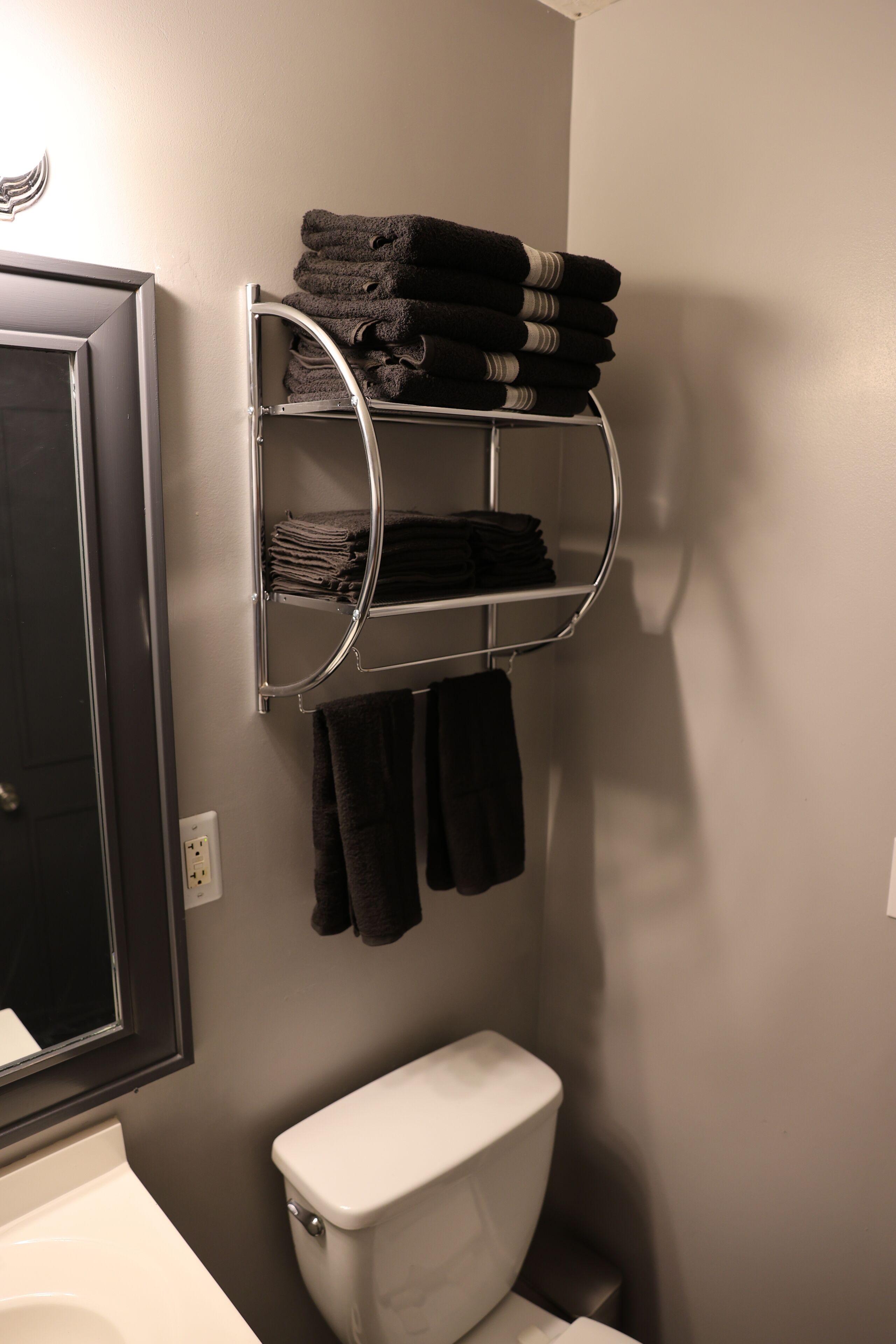 Een badkamer met een wit toilet, een handdoekrek met opgevouwen handdoeken en een spiegel boven het toilet.