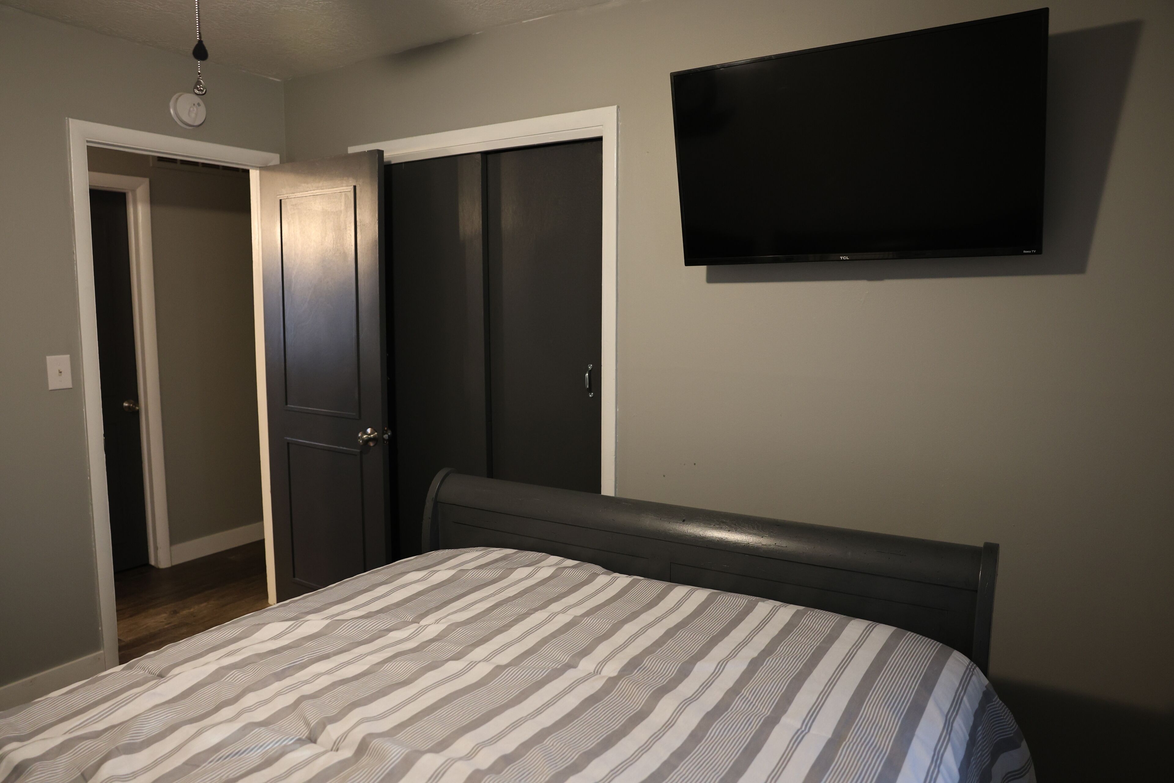 A bedroom with a bed, a TV mounted on the wall, and a door leading to another room.