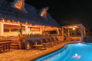 A poolside area with lounge chairs, a thatched-roof structure, and a pool.