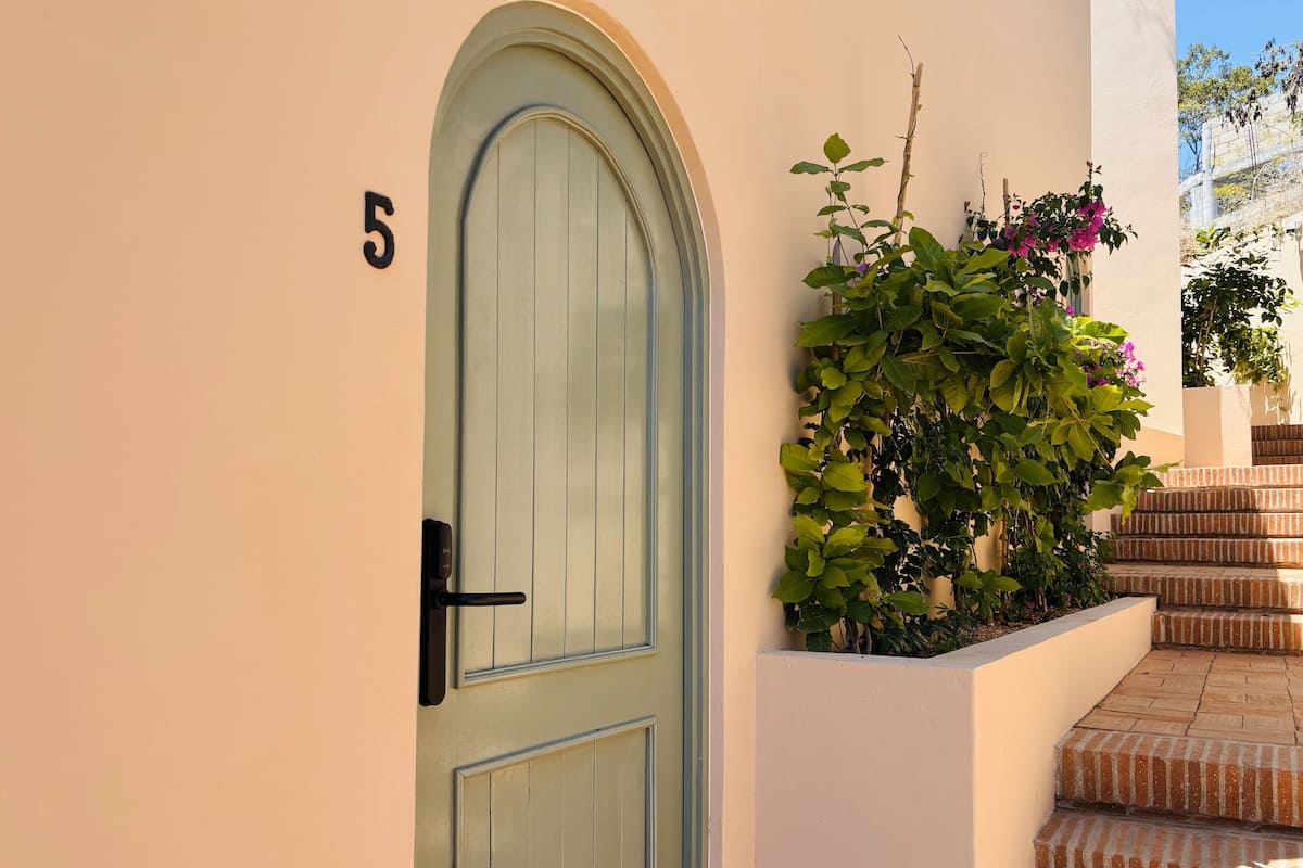 Ein Gebäude mit einer grünen Tür, der Hausnummer 5 und einer Treppe aus Ziegelsteinen, die zu einer weißen Wand mit Pflanzen und Blumen führt.