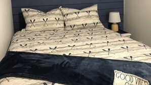 A bed with a navy blue headboard, a quilted bedspread with a leaf pattern, and a dark blue throw blanket. - Charming shipping container home with lake view and boat ramp. (Cookson)