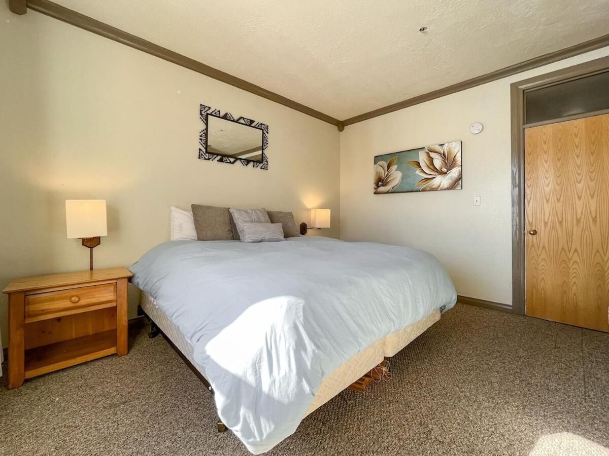 A bedroom with a large bed, a nightstand, a mirror, and a door.