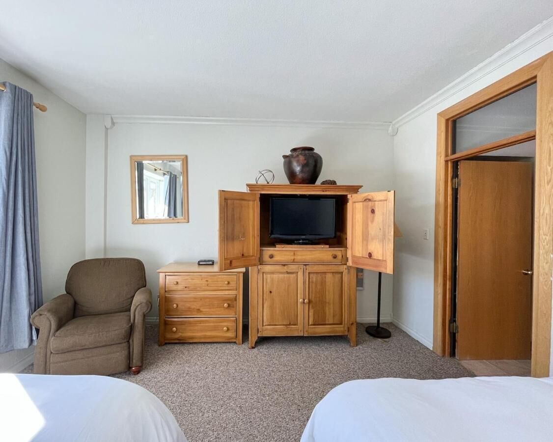 Une chambre d’hôtel comprenant un lit, une chaise, une armoire en bois avec un téléviseur et une porte.