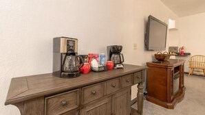 Ett köksutrymme med en kaffebryggare, en brödrost och en mikrovågsugn på en bänkskiva i trä. I bakgrunden finns en flätstol och en tv som är monterad på väggen.