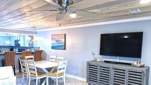 A living room with a dining area, a large flat-screen TV, and a ceiling fan. - 11 Drift - 2BR $700+ in freebies incl golf, pool (Miramar Beach)