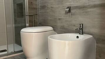 Ein modernes Badezimmer mit Toilette und Bidet, Holzwandfliesen und einer Duschkabine aus Glas.