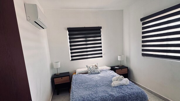Una camera da letto con un letto, due comodini, una finestra con persiane e un condizionatore.