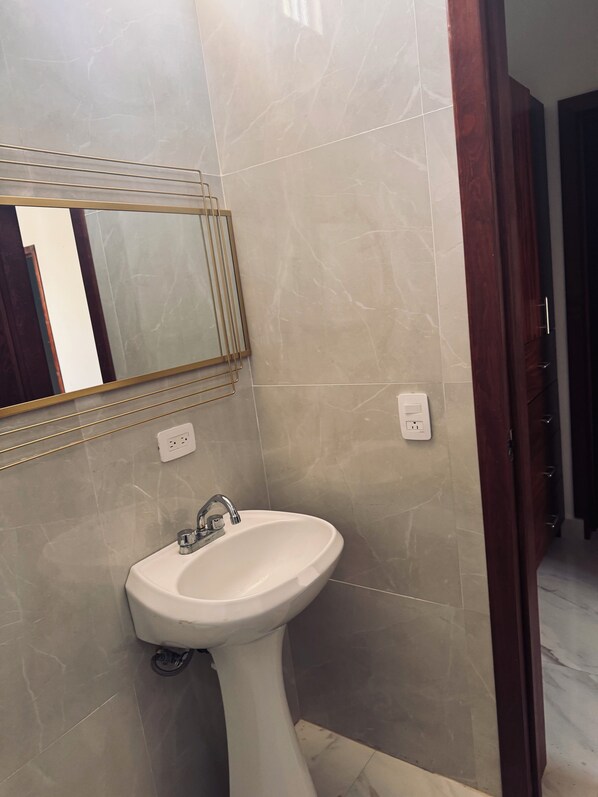 A bathroom with a white pedestal sink, a mirror with a gold frame, and a wooden door.