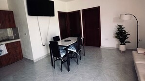 Un soggiorno moderno con zona pranzo, una TV a schermo piatto montata a parete, un divano, una pianta in vaso e una lampada da terra.