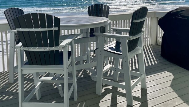 Een terras met een ronde tafel en vier Adirondack-stoelen gericht op de oceaan.