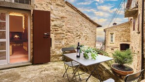 A stone building with a table and chairs outside, a bottle of wine, and potted plants. - The Crusher (whirlpool) (Rivalto)