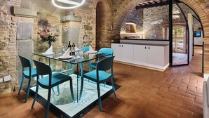 A rustic kitchen with stone walls, a glass table, and blue chairs. - The Crusher (whirlpool) (Rivalto)