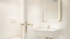 Et badeværelse med et hvidt toilet, en vask og et spejl.