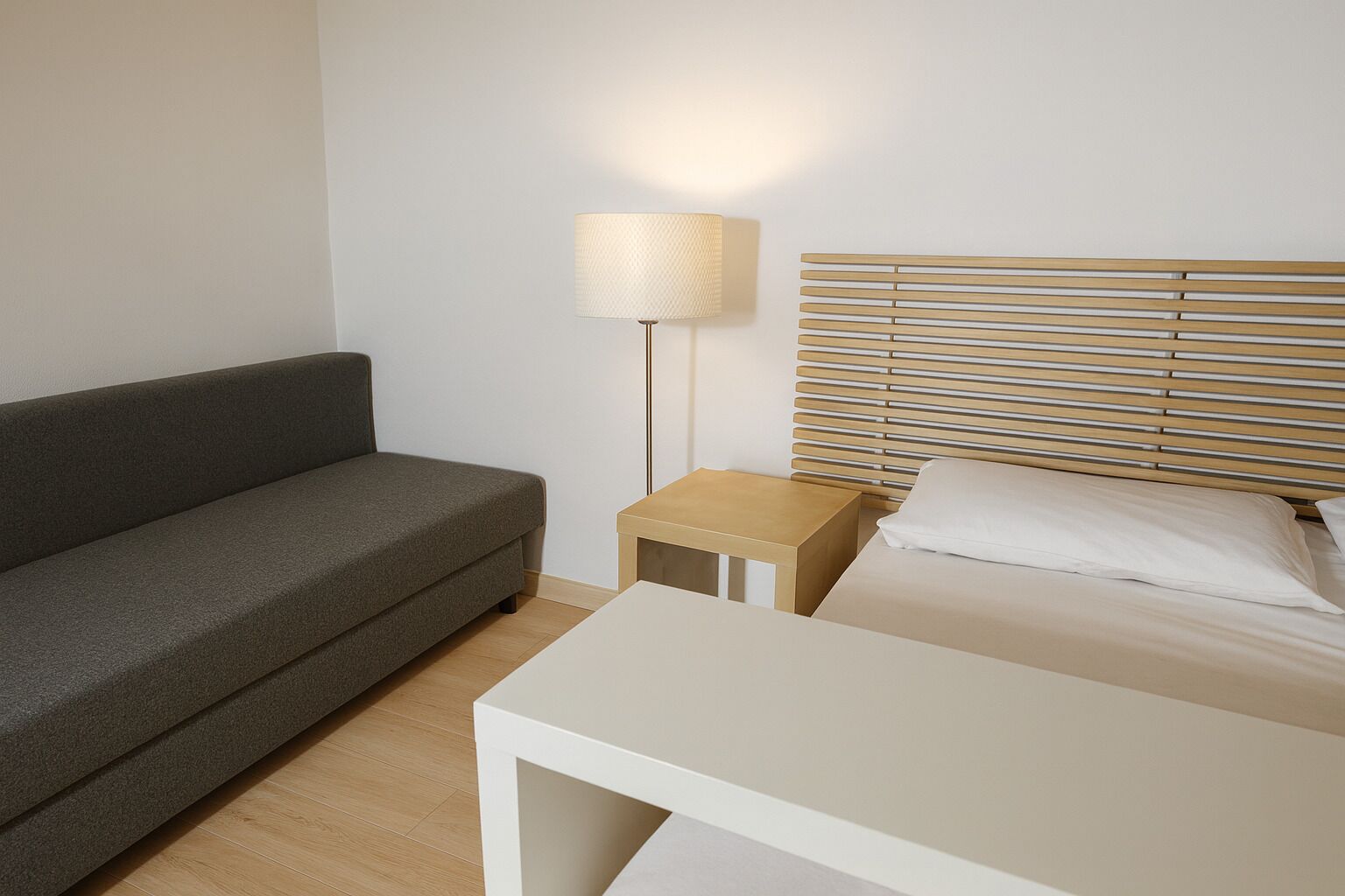 A room with a bed, a sofa, a small table, and a lamp.
