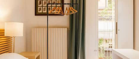 Ein Hotelzimmer mit Bett, Nachttisch, Lampe, Heizkörper, Vorhang und einer Tür, die auf einen Balkon führt.