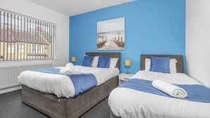 A hotel room with two beds, a large window with a view of buildings, a painting on the wall, and a ceiling light.