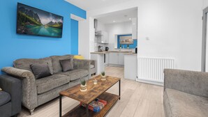 A modern living room with a grey sofa, a coffee table, and a painting of a mountain landscape.