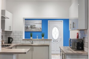 Eine moderne Küche mit weißen Schränken, einer blauen Akzentwand, einem Gemälde eines Bootes und einer Tür mit rundem Fenster.
