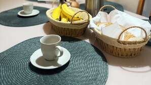 A dining table with a white cup, a basket of bananas, a thermos, and a woven basket with napkins.
