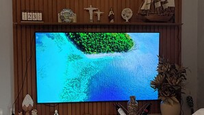 A flat-screen TV mounted on a wooden wall with a shelf above displaying various decorative items.