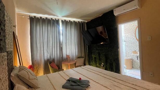 A bedroom with a large bed, a flat-screen TV mounted on the wall, and a sliding glass door leading to a balcony.