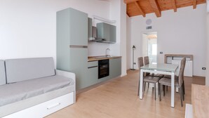 Une cuisine moderne dotée d’un four encastré, d’un coin repas avec une table et des chaises en verre, et d’un canapé muni de tiroirs de rangement.
