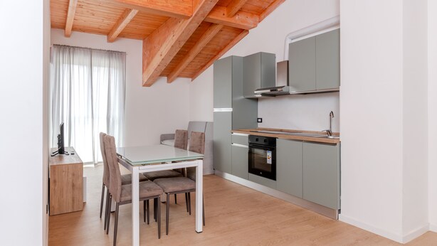 A modern kitchen with a wooden ceiling, a dining table with chairs, and a built-in oven.