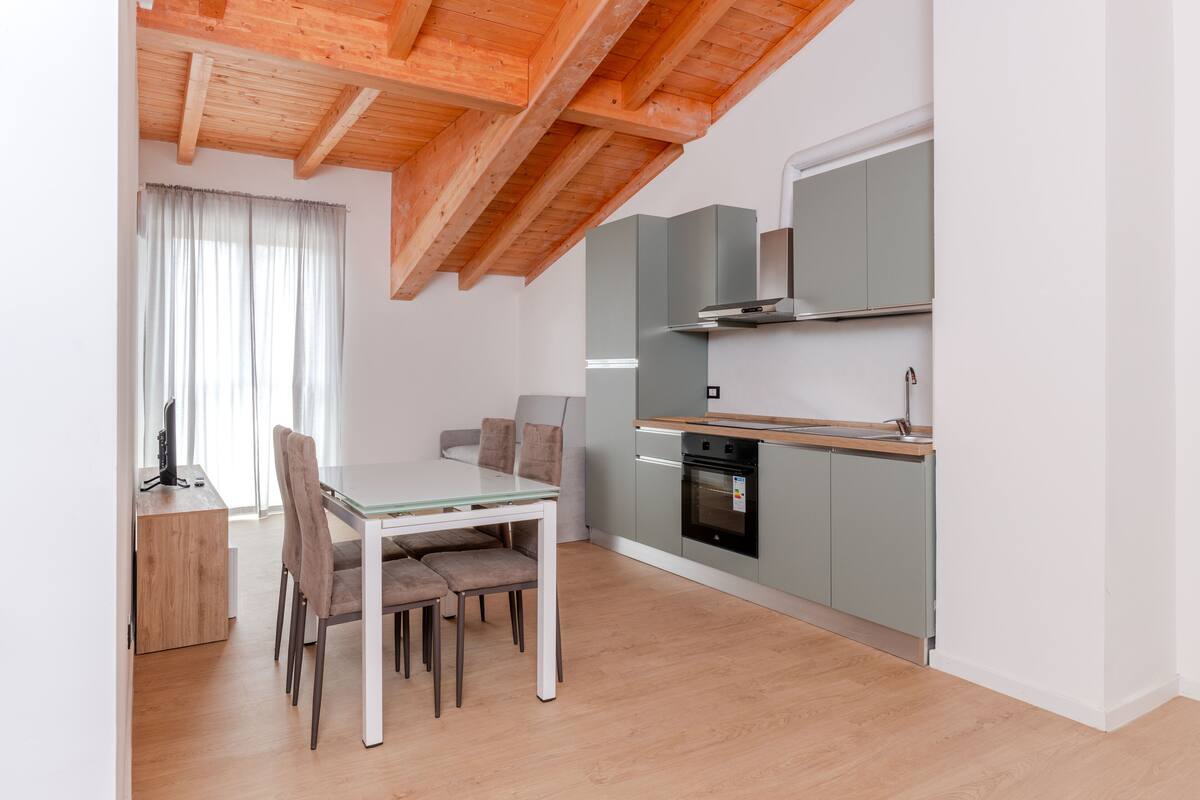 A modern kitchen with a wooden ceiling, a dining table with chairs, and a built-in oven.