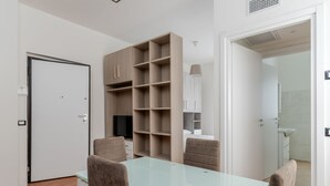 Un salon moderne avec une table à plateau en verre, deux fauteuils marron, un téléviseur et des étagères intégrées.