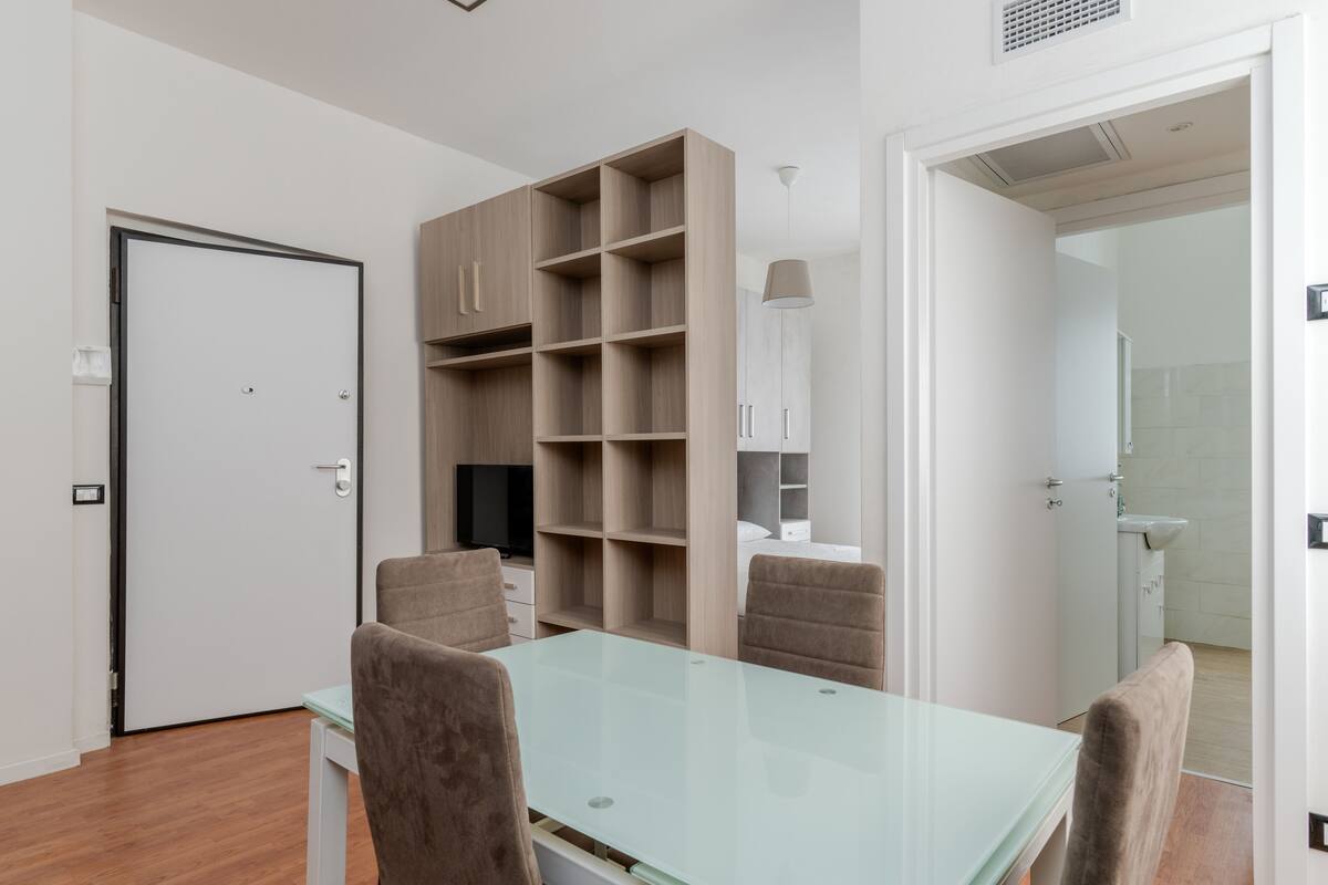 A modern living room with a glass-top table, two brown chairs, a TV, and built-in shelving.
