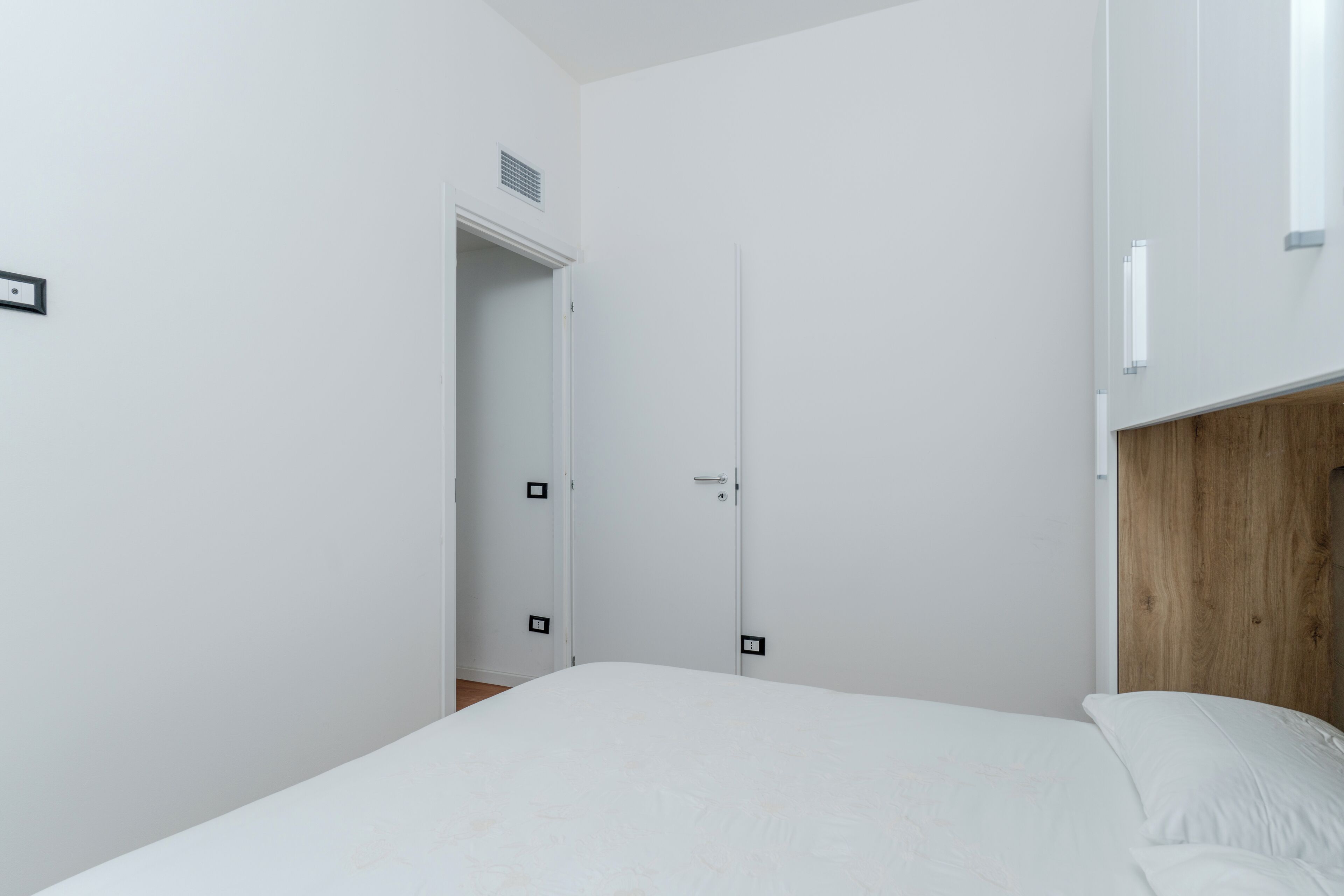 Ein Schlafzimmer mit einem Bett, einem hölzernen Kopfteil, einer weißen Tür und einer weißen Wand.