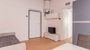 A modern room with a bed, a TV on a white cabinet, a heater, and a door.