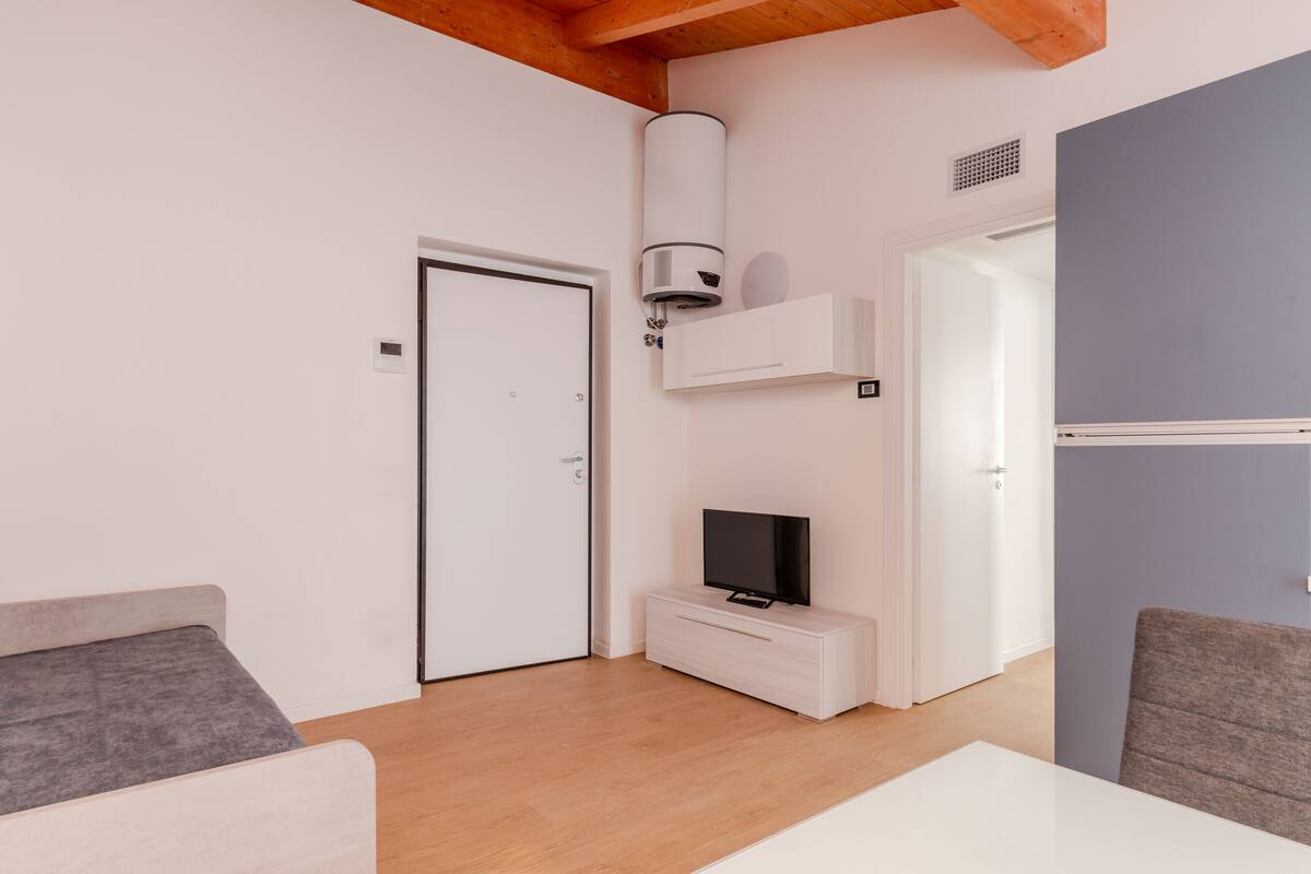 A modern room with a bed, a TV on a white cabinet, a heater, and a door.