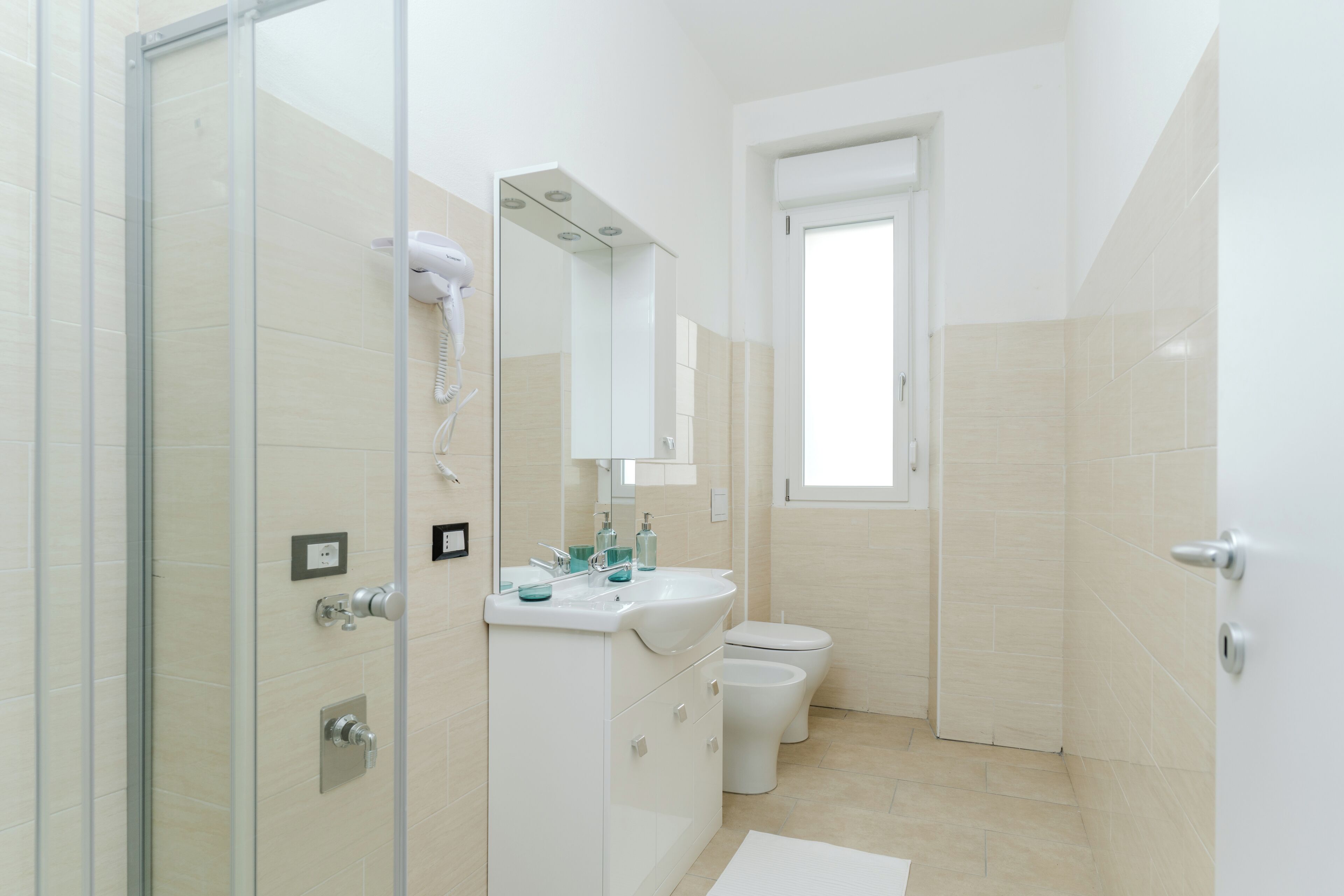 Ein modernes Badezimmer mit einer Duschkabine aus Glas, einem weißen Waschbecken mit Spiegel und einer Toilette.