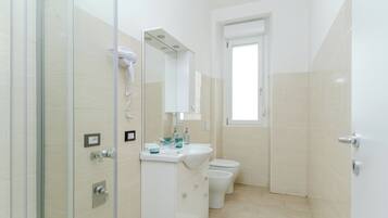 Ein modernes Badezimmer mit einer Duschkabine aus Glas, einem weißen Waschbecken mit Spiegel und einer Toilette.