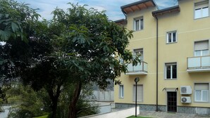 A multi-story residential building with balconies, a paved courtyard, and a large tree.