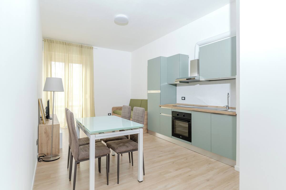 A modern kitchen with a built-in oven and a dining area with a glass table and cushioned chairs.
