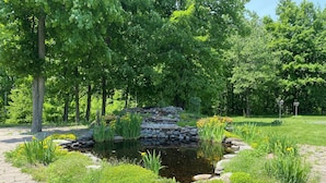 A serene garden with a pond, surrounded by lush greenery and stone structures.