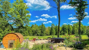 A wooden cabin with a patio area, surrounded by lush greenery and a clear blue sky.